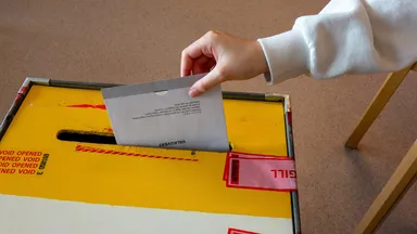 A hand dropping a folded ballot paper into a sealed ballot box