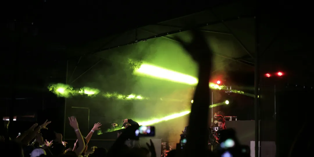 Silhouetted concertgoers raise their hands toward a brightly lit stage.
